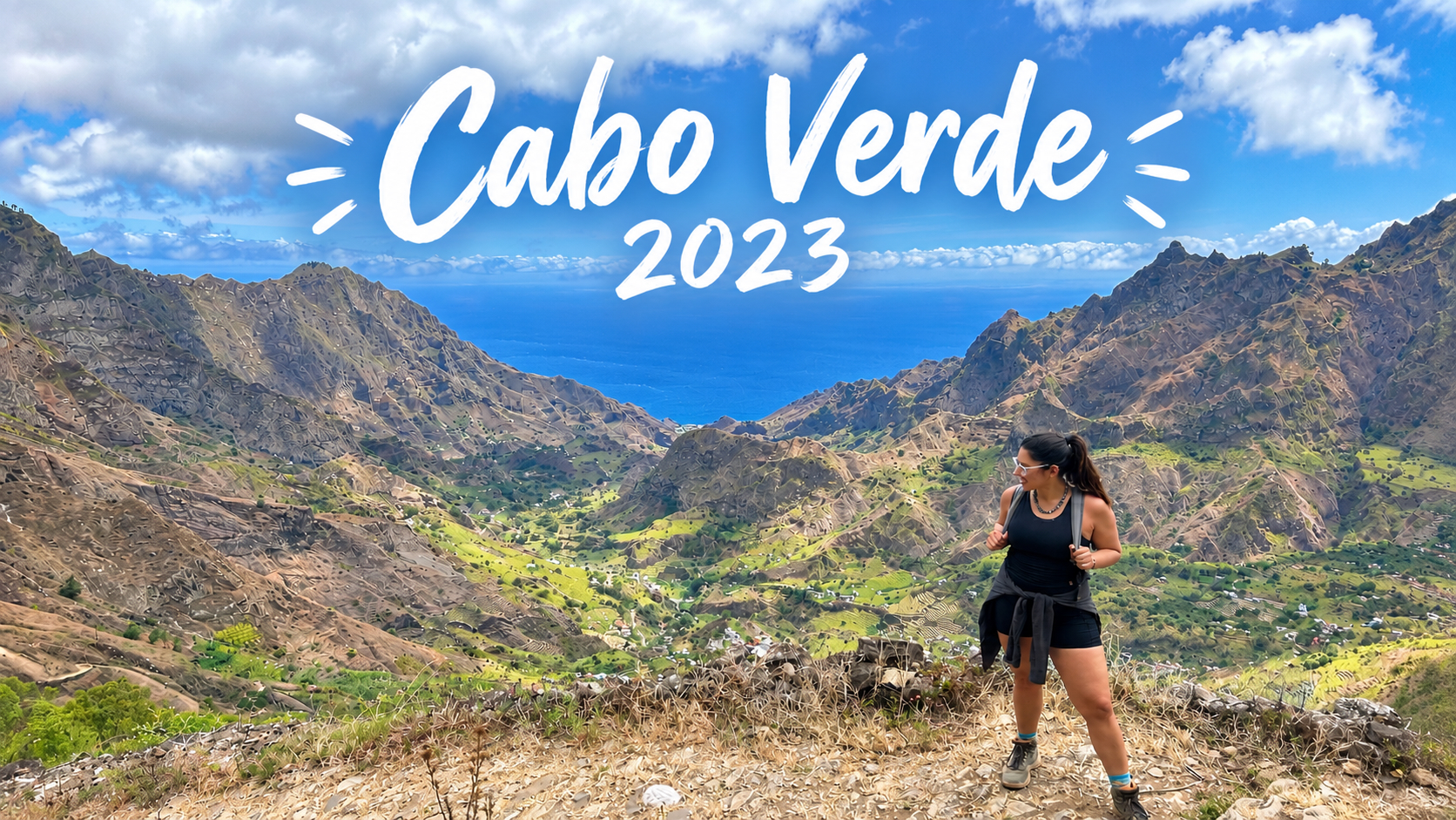 Cabo Verde 2023: Gizela standing on a mountain trail above a green valley that opens onto the Atlantic Ocean.